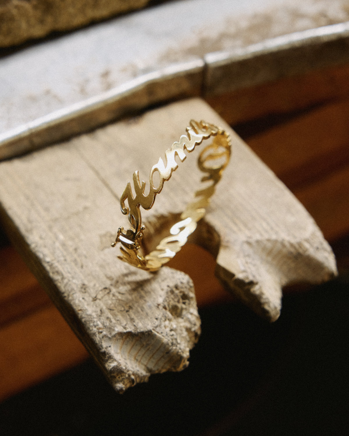18k yellow gold name bracelet with names in script, resting on a jeweler's wooden bench pin.