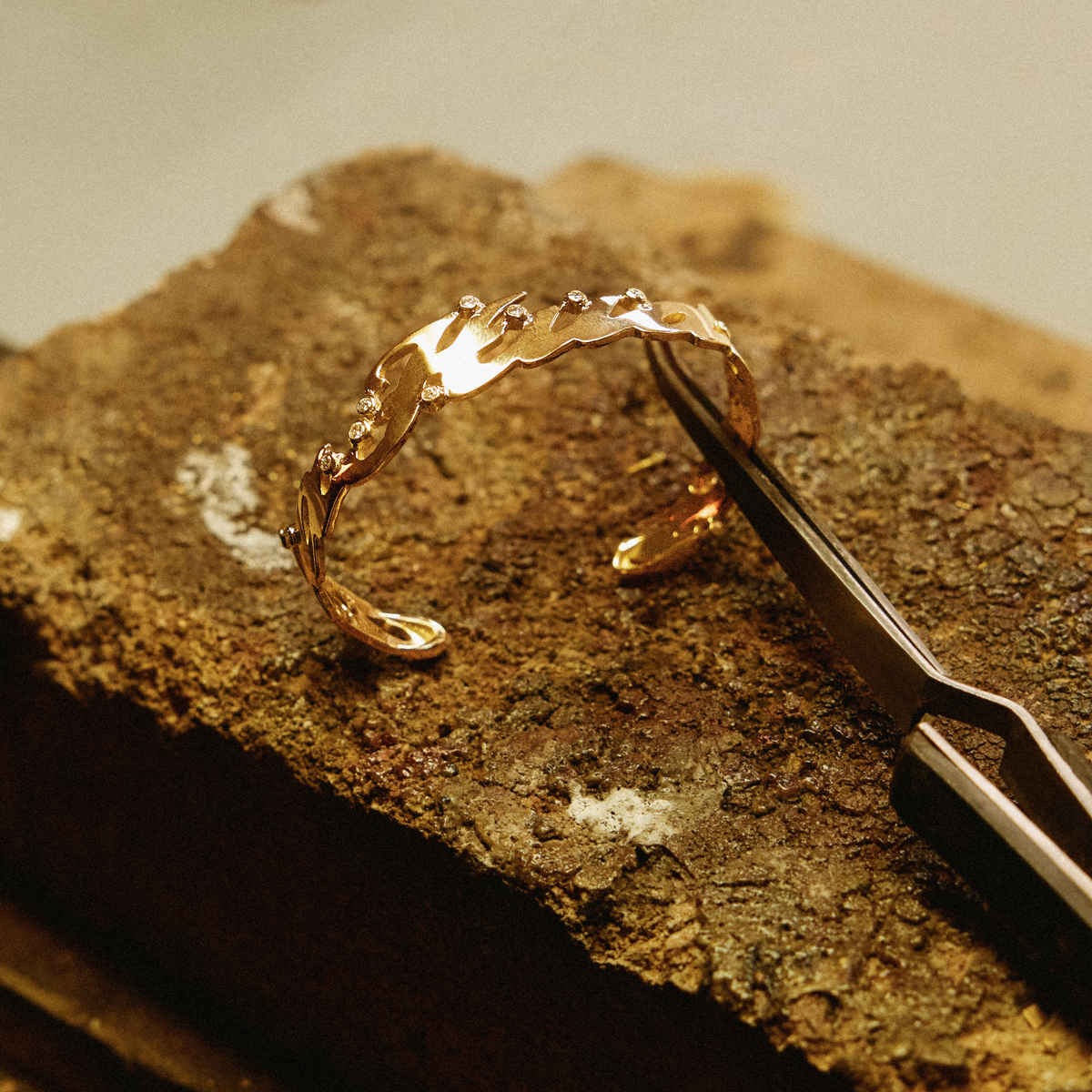 18k gold name cuff with small diamonds set along the letters, held with tweezers on a soldering block