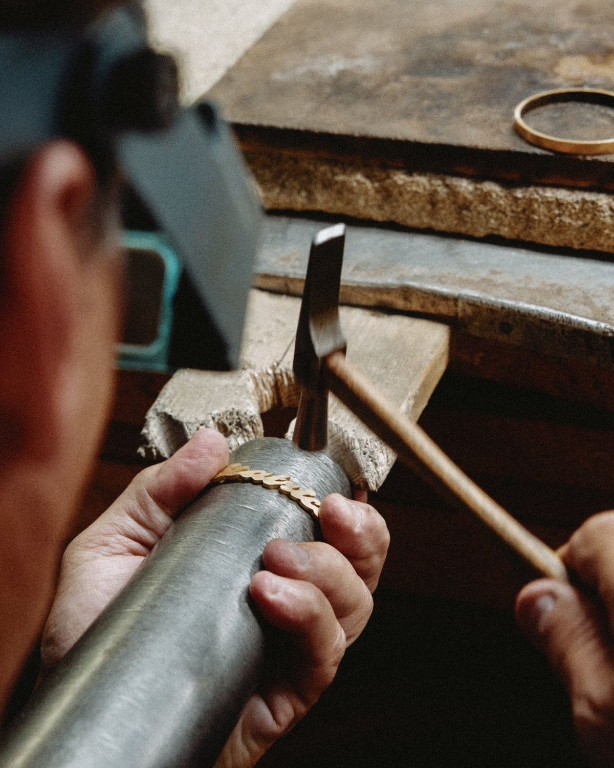 A goldsmith shapes a gold name bracelet around a steel mandrel with a hammer