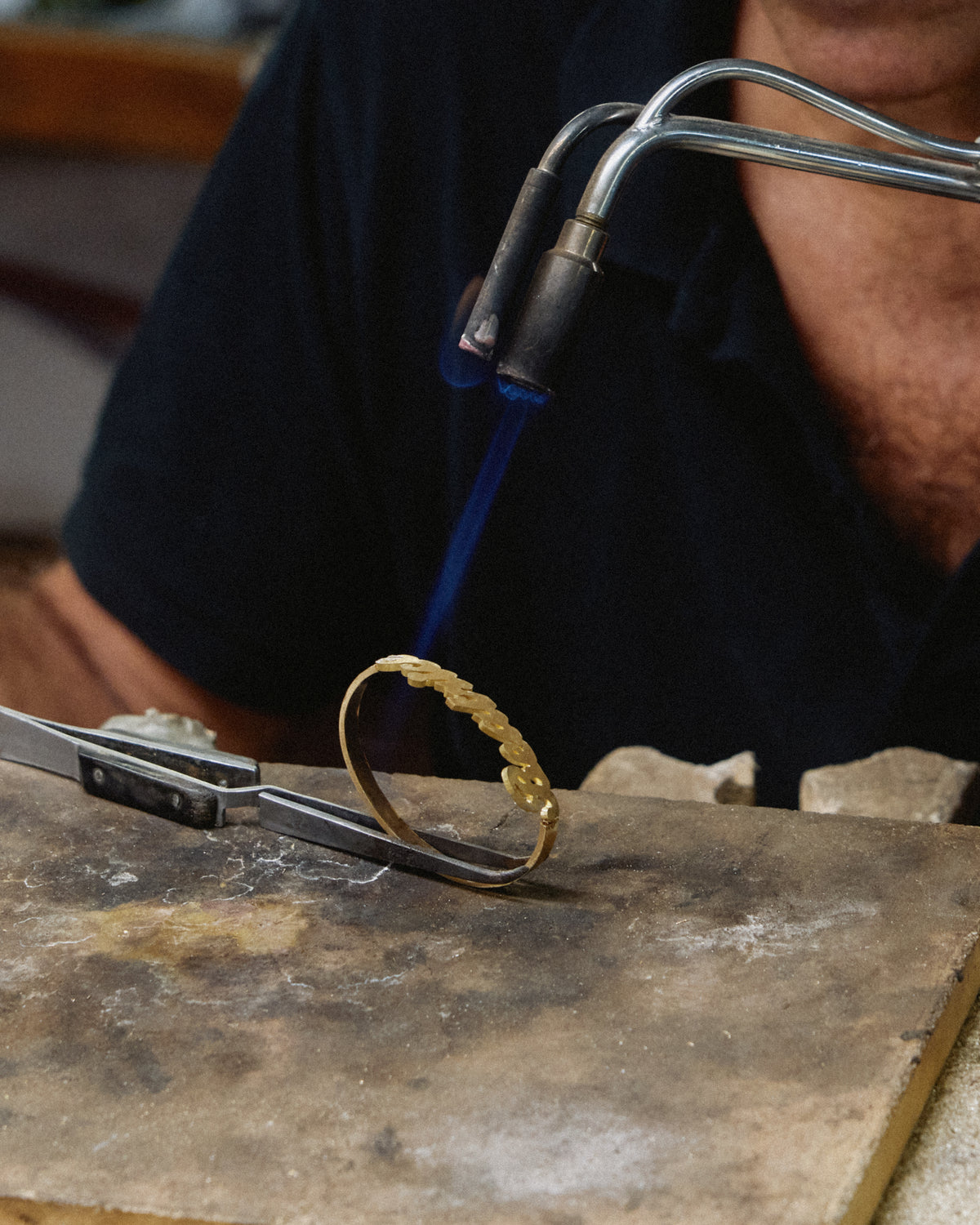 A gold name bracelet being soldered with a torch in the workshop
